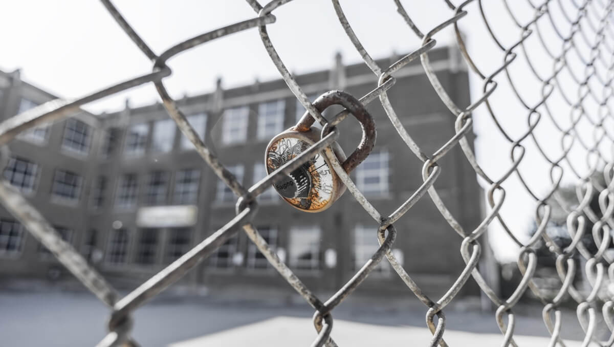 Rusty and broken combination lock attached to chain link fence outside of large urban school