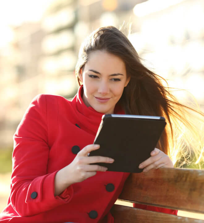 Woman red coat- reading tablet in park